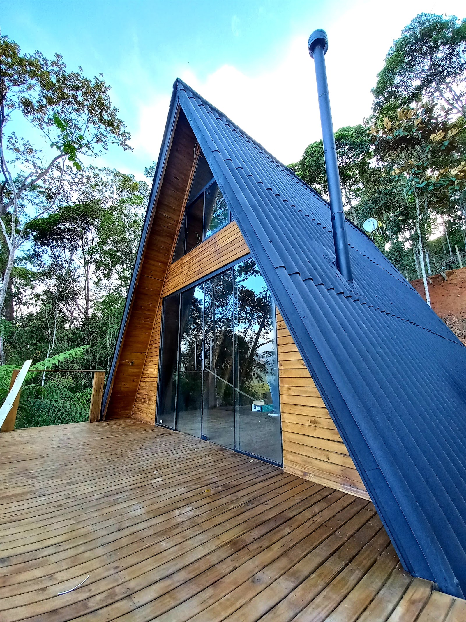 Cabana A-frame de telhado azul e parede de vidro, com deck de madeira, no meio da mata