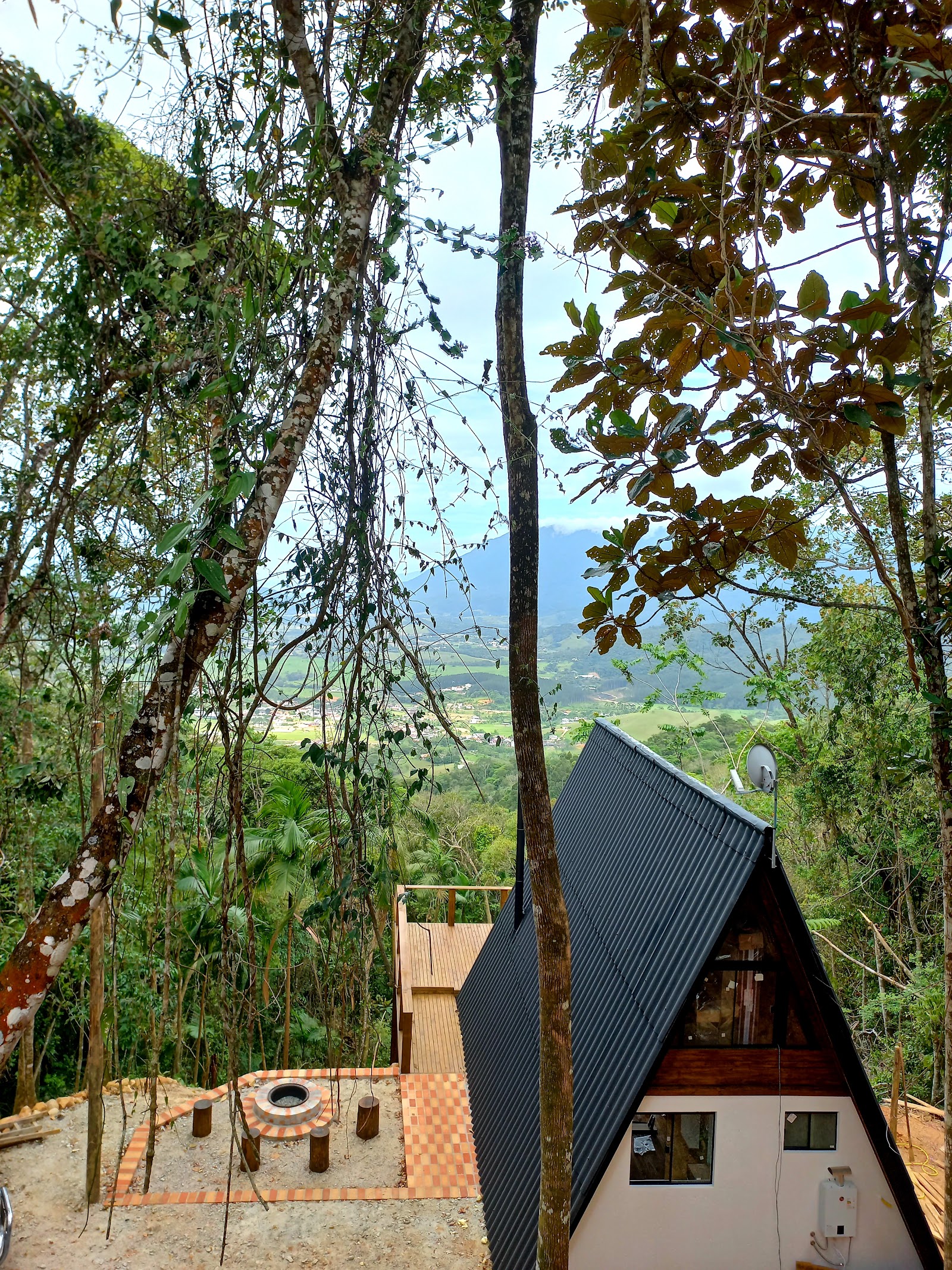 Vista do vale e da baía entre as árvores, com o telhado de uma das cabanas embaixo