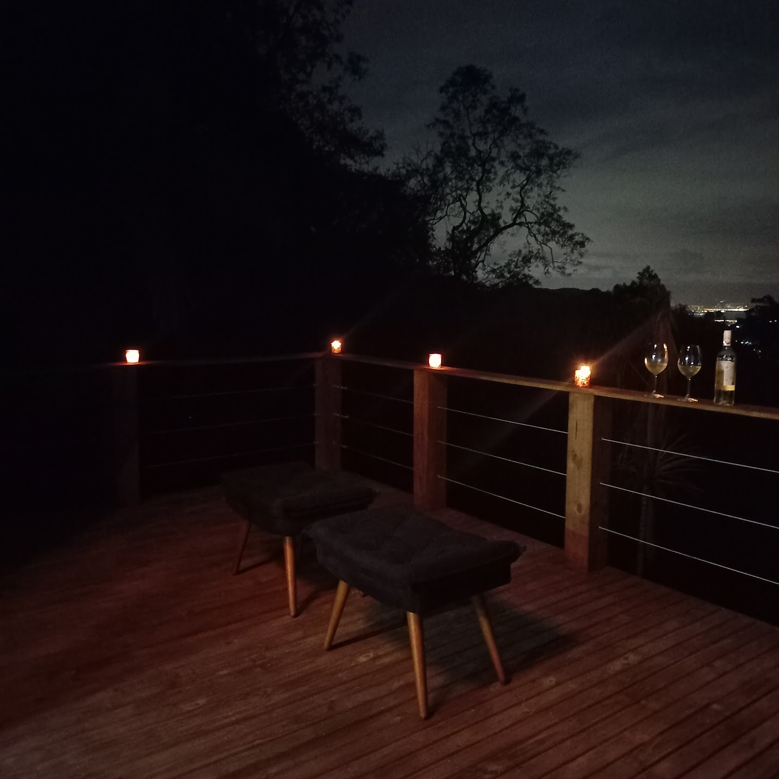 Deck da cabana à noite, com luzes baixas e duas taças